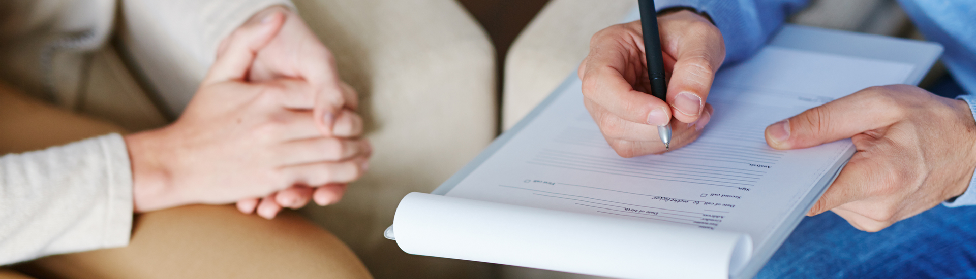 Hands of psychiatrist filling in medical document with patient near by