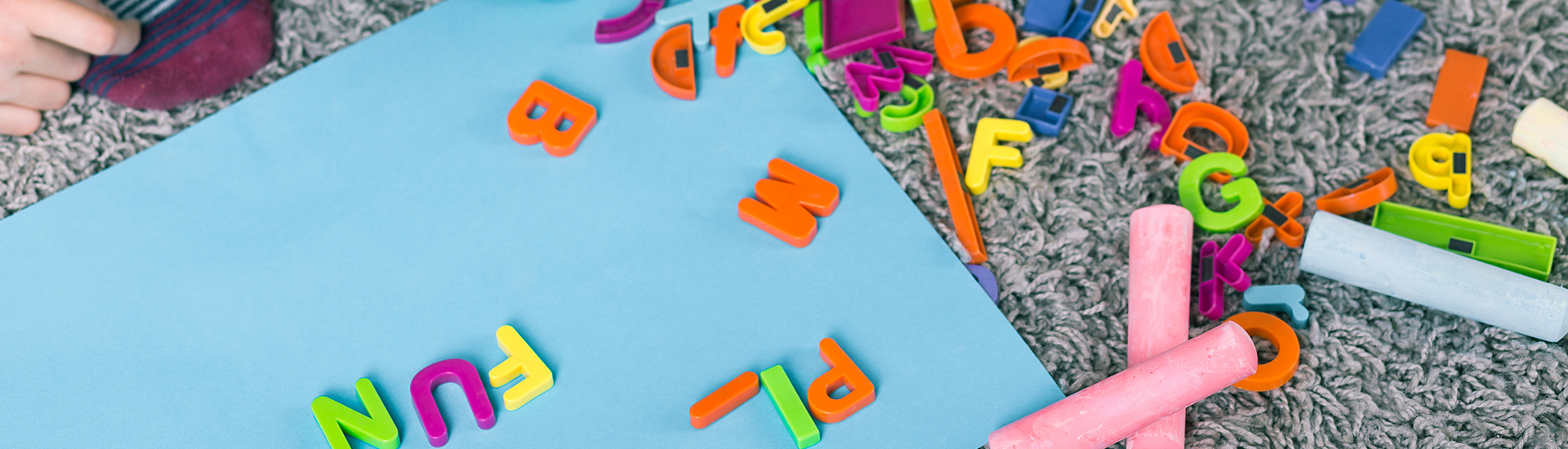 Toy letters and colorful chalk lying on carpet, close up, panorama.